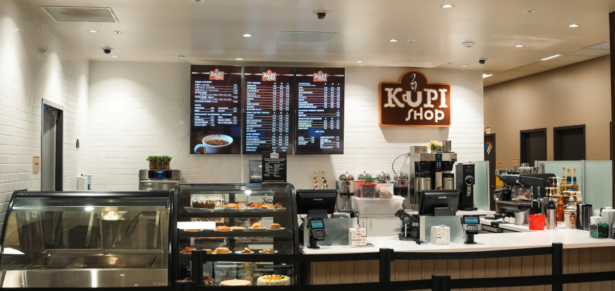 Interior of Kupi Coffee Shop at Shelee's Travel Center featuring a menu board, pastry display case, and coffee brewing equipment.