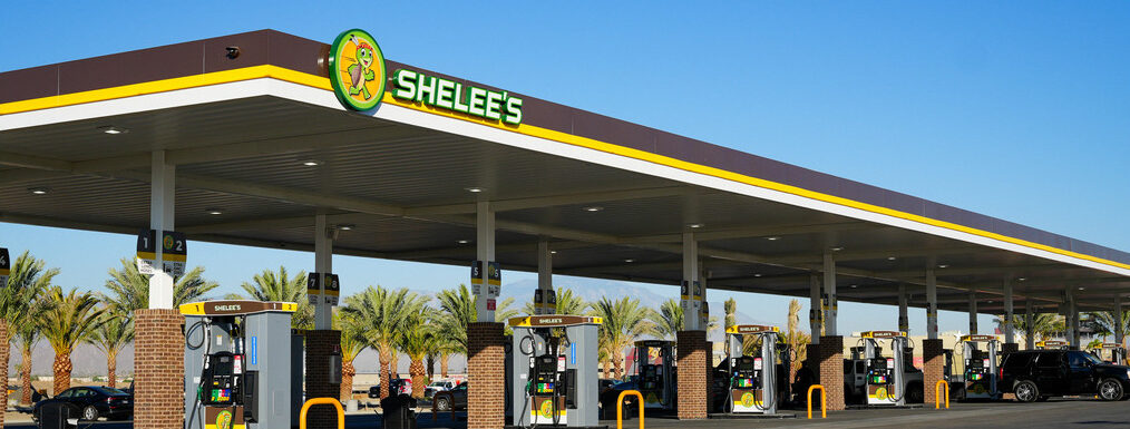 Shelee's Travel Center fuel stations with over multiple pumps under a large canopy, offering a convenient and spacious fueling experience with palm trees in the background.